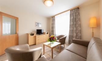 A cozy living room with a sofa and two armchairs. A table with a floral arrangement and a television are in the room.