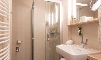 A modern bathroom with a glass shower cubicle and an elegant sink. The walls are light and the furnishings are simple and functional.