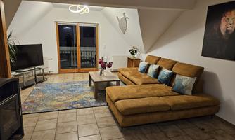 A modern living room with a beige couch and a television. Large windows let the light in and a rug adds to the coziness.