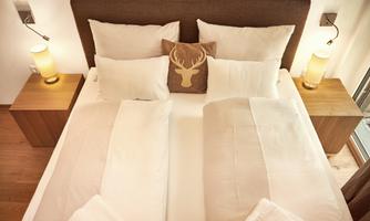 A cozy bedroom with a double bed and many pillows. Next to the bed are two nightstands with lamps.