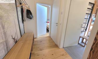 A bright hallway with wooden flooring and a coat rack. In the background, more doors can be seen.