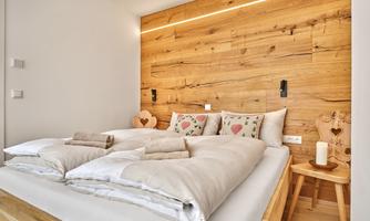 A cozy bedroom with a wooden panel as a headboard. The bed is decorated with white blankets and colorful pillows.