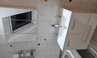 A modern bathroom with a white sink and a large mirrored cabinet. The walls are tiled, and there is a bathtub on the left side.