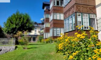 A sunny garden with yellow flowers and a beautiful building in the background. The green lawn and the clear sky create an inviting atmosphere.