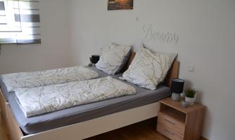 A cozy bedroom with a double bed and bright bedcovers. Next to the bed is a bedside table with a lamp and a small plant.