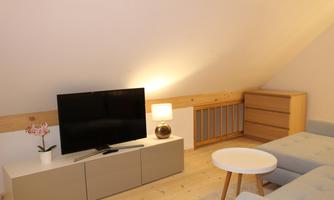 A cozy living room in the attic with a television and a white chest of drawers. The room is bright and furnished in a modern style.