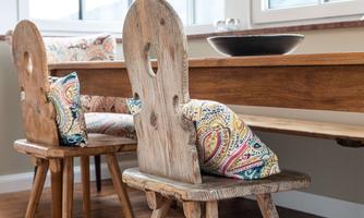 A rustic wooden table with two chairs and colorful cushions. The bright surroundings create an inviting atmosphere.