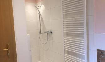 A bright shower with white tiles and modern fixtures. A towel radiator is attached to the wall.