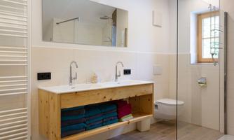 A modern bathroom with a wooden vanity and two sinks. The shower is separated by glass walls and large towels are neatly arranged.