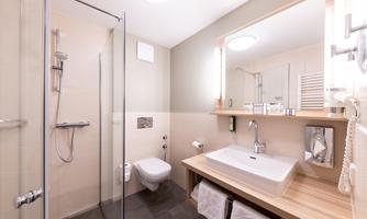 A modern bathroom with a shower, sink, and toilet. The walls are in neutral colors and there are wood details.