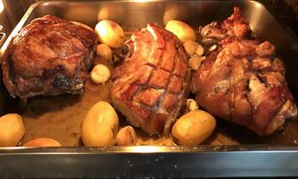 A metal baking dish with three large pieces of roasted meat and potatoes is visible. The meat has a crispy crust and is swimming in a spicy broth.