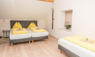 A cozy bedroom with two beds and a single bed. The beds are adorned with yellow pillows and fresh flowers.