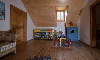 A cozy playroom with a wooden floor. There is a playhouse and colorful toys on a shelf.