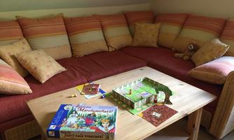 A cozy living room with a large, inviting couch and many pillows. Various board games and a play mat are on the table.
