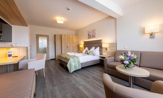 A modern hotel room with a double bed and a cozy seating area. The decor is bright and inviting.