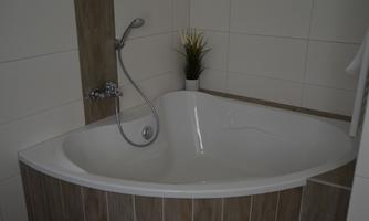 A modern designed corner bathtub in a bright bathroom. There is a potted plant that creates a cozy atmosphere.
