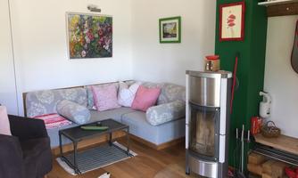 A cozy living area with a gray and white sofa and colorful cushions. In the background, there is a modern fireplace and some decorative pictures on the wall.