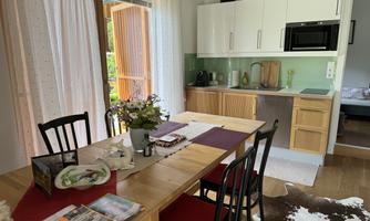 A bright kitchen with a dining table and black chairs. Flowers and some magazines are on the table.