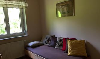A cozy room with a daybed and several pillows. Natural light shines through the window, creating a bright atmosphere.