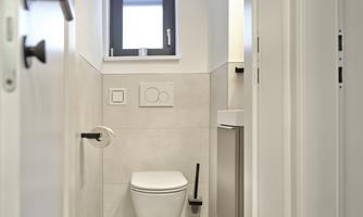 A modern bathroom with a toilet and a small window. The walls are bright tiled and the space appears clean and functional.