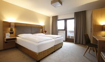 A modern hotel room with a double bed and warm wood tones. Large windows ensure plenty of daylight and a cozy atmosphere.