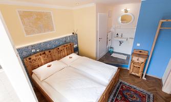A cozy room with two beds and a rustic wood design. The walls are painted in soft colors and there is a small bathroom area.