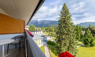 A beautiful balcony with a view of mountains and green trees. The flowers on the railing add a colorful touch.