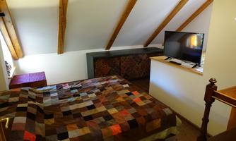 A cozy bedroom with a bed that has a colorful blanket. There is a television and a window that lets in daylight.