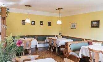 A cozy restaurant with bright walls and tables covered with white tablecloths. Various pictures hang on the walls, and there is a green seating area.