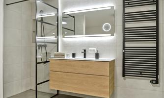A modern bathroom with a glass shower and a wooden sink. The walls are in neutral tones and a lighted mirror complements the design.