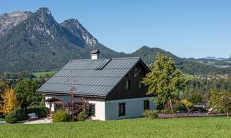 A charming house in a rural setting with green grass and trees. In the background, majestic mountains can be seen.