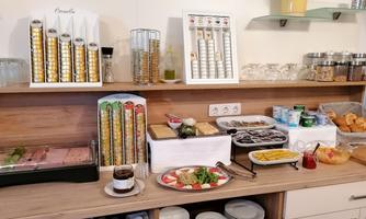 A buffet with various dishes and drinks. You can see salads, cold cuts, rolls, and numerous glasses.
