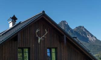 A wooden house with a deer antler attachment on the wall. In the background, there are large mountains under a clear blue sky.
