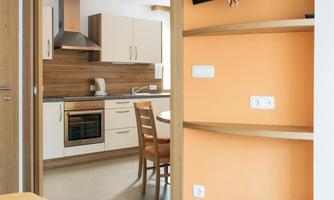 A modern room with a visible kitchen area. The walls are painted in a friendly orange, and a television is mounted on the wall.