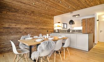 A modern kitchen with a wooden table and elegant chairs. The room has a warm atmosphere with wooden ceilings and walls.