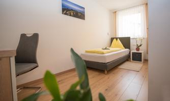 A bright room with a single bed and yellow bed linen. A desk chair and a small nightstand are also available.