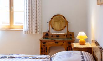 A cozy bedroom with a wooden table and a mirror. Next to the table stands a lamp with warm light.