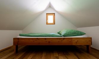 A cozy bedroom with a wooden bed and checkered pillows. The roof is slanted, and a small window lets in natural light.