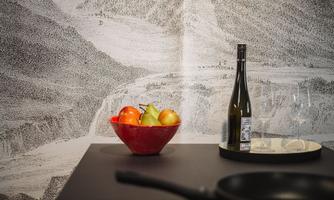 A modern kitchen setup with a red fruit bowl containing apples and pears. In the background, there is an artistic wall design, and in the foreground, there are a wine bottle and glasses.