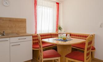 A cozy kitchen with a round wooden table and red benches. Bright windows let in plenty of light and create an inviting atmosphere.