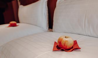 A cozy hotel room with two beds and fresh apples on red coasters. The bedding is white and clean.