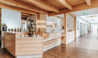 A modern reception area with wooden paneling and bright lighting. The room has an inviting atmosphere and leads into a long hallway.