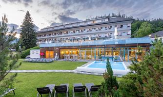 A modern hotel with a beautiful garden and a pool. The facade is equipped with large windows and invites relaxation.