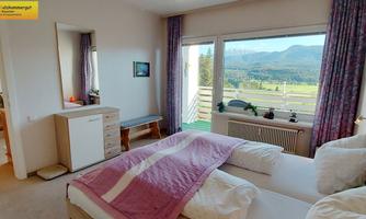 A cozy bedroom with two beds and large windows that offer a view of the landscape. The walls are painted light and decorated with curtains.