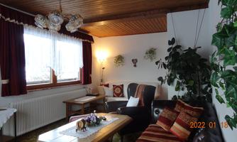 A cozy living room with a couch and a table. There are plants and windows that let in plenty of light.