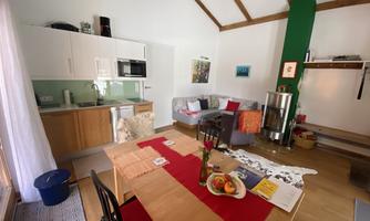 A cozy living area with a modern kitchen and a dining table. The room is brightly and cheerfully furnished, with a warm color palette.