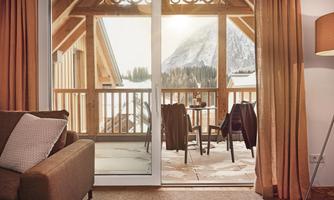 A cozy room with a view of a balcony and the mountains. The room is bright and welcoming, with warm decoration.