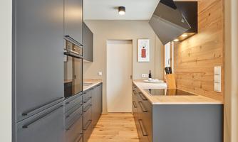 A modern kitchen with gray cabinets and wooden walls. It is well-lit and has a practical layout.