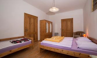 A simple bedroom with two beds and a wardrobe. The walls are white and the floor is made of wood.