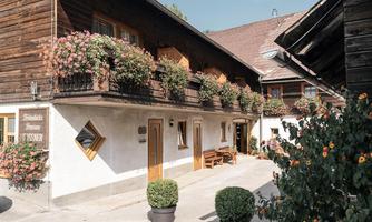 A charming, traditional wooden house with blooming flower boxes at the windows. The courtyard is inviting and well-maintained.
